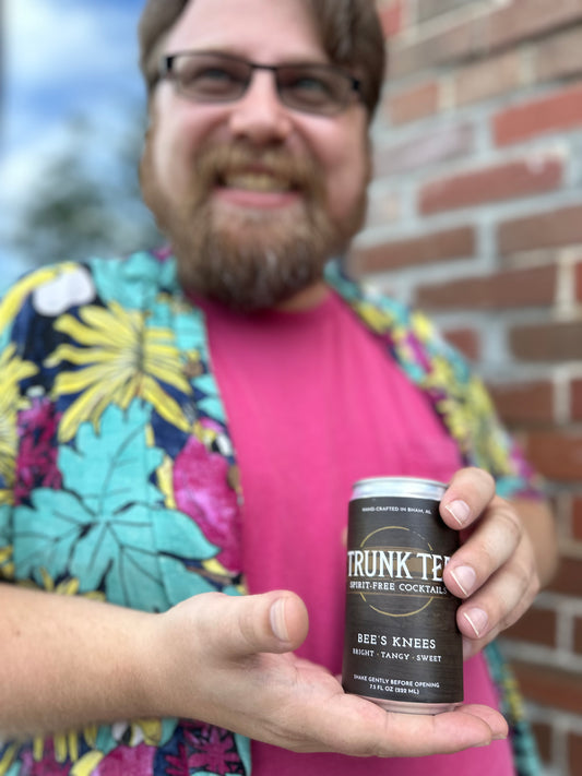 A can of Trunk Tea Spirit-Free Bee's Knees Mocktail, being presented by a male smiling in a Hawaiian shirt
