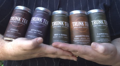 All five flavors of Trunk Tea Spirit-Free Cocktails are cradled across a person's arms. Flavors are Cosmo, Aviation, Bee's Knees, Amaretto Sour and Caipirinha 